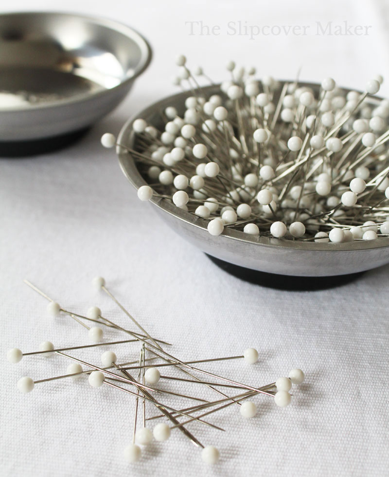 Straight pins with white heads sitting in silver bowl.