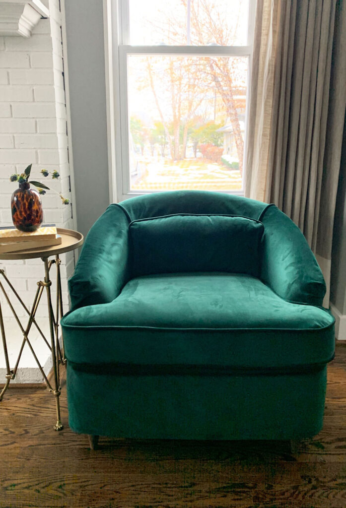 Emerald green velvet chair in front of window.