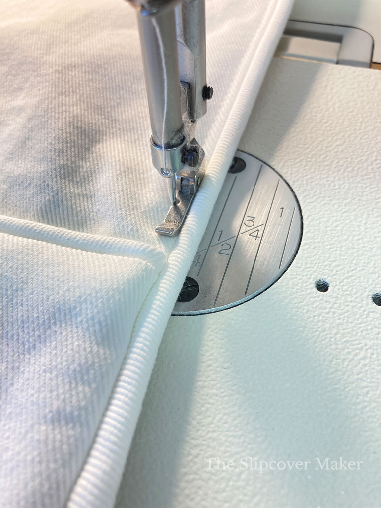 Sewing machine stitching welt cord hem on slipcover.