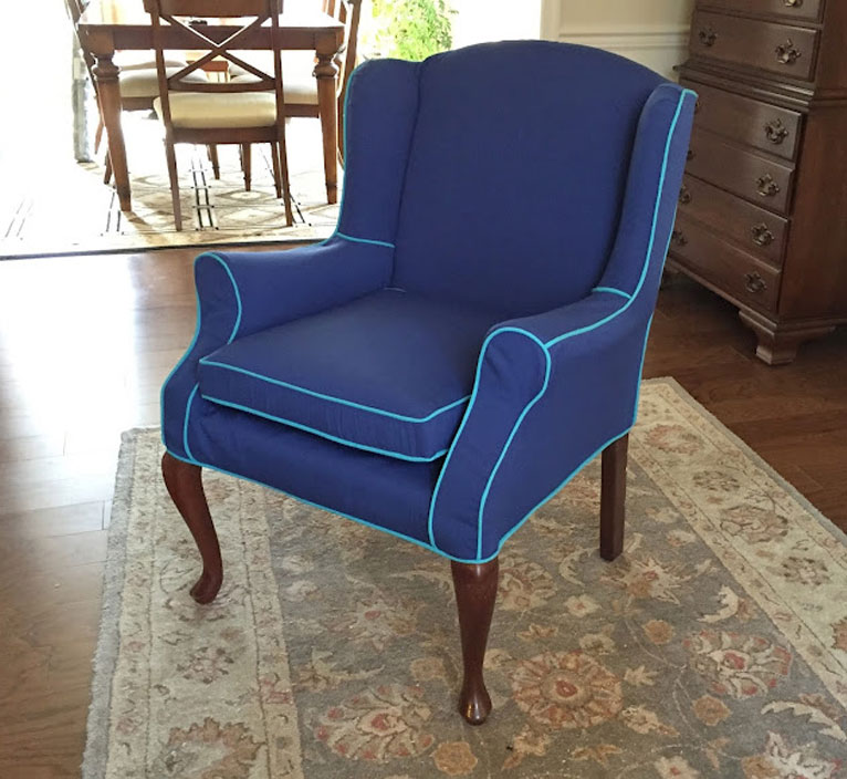 Wingback chair with a blue slipcover and aqua piping.